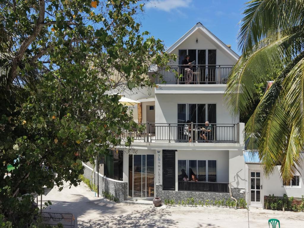 a white house with people sitting on a balcony at Alma Maldiva, Beach Hotel in Ariyaddu