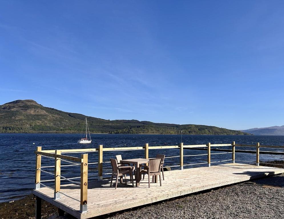 a wooden dock with chairs and a table on the water at Mid- Village Croft in Cairndow