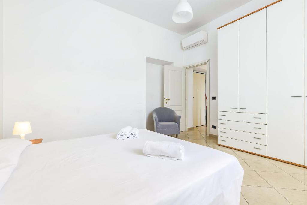 a white bedroom with a large bed and a chair at Hostdomus - Villa Emma - Zoe e Ascanio in Alassio