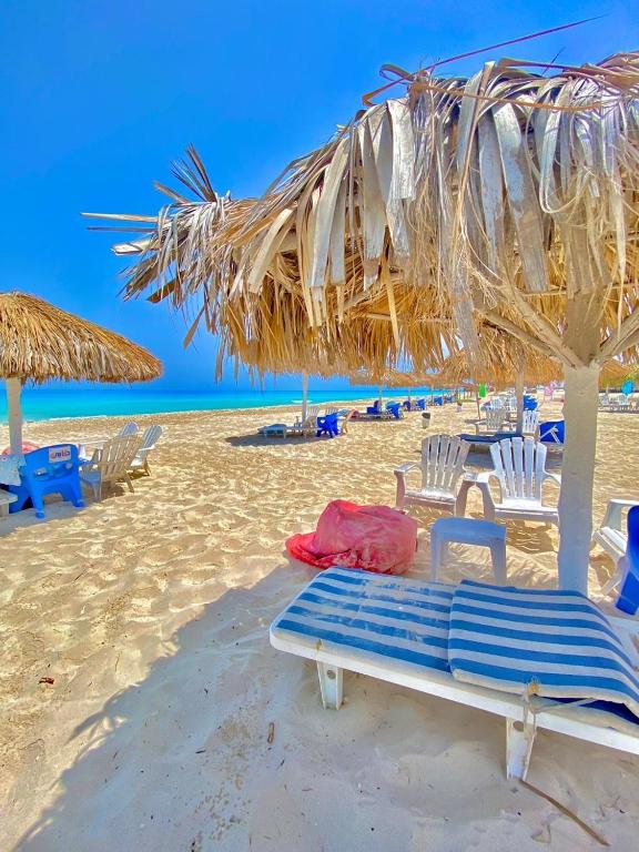 a beach with chairs and a straw umbrellas and a bench at casabianca north coast villa code 112 in Dawwār Muḩammad Abū Shanab