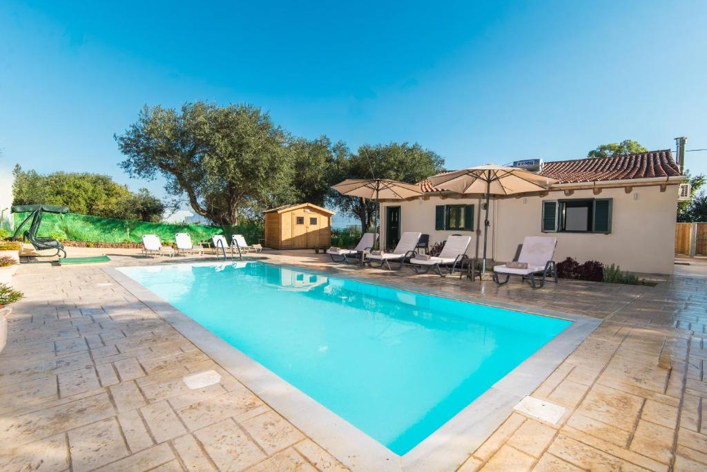 a pool with chairs and umbrellas next to a house at Villa Taxiarchis by Corfuescapes in Benitses