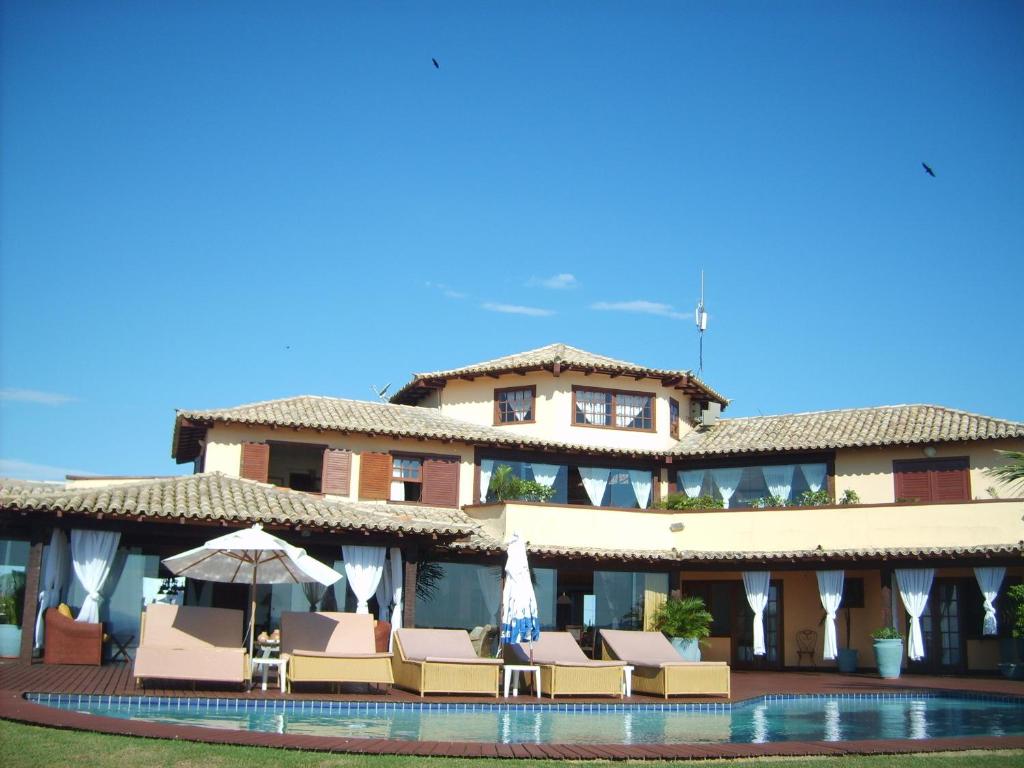 a large building with a pool and chairs and an umbrella at Pousada Porta Do Céu in Búzios