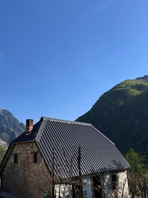 a stone building with a metal roof with mountains in the background at Oda Pisha Theth in Grumas