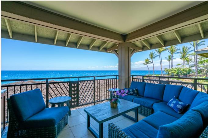 a porch with blue couches and a table and the ocean at Oceanfront Condo Halii Kai 14D in Waikoloa