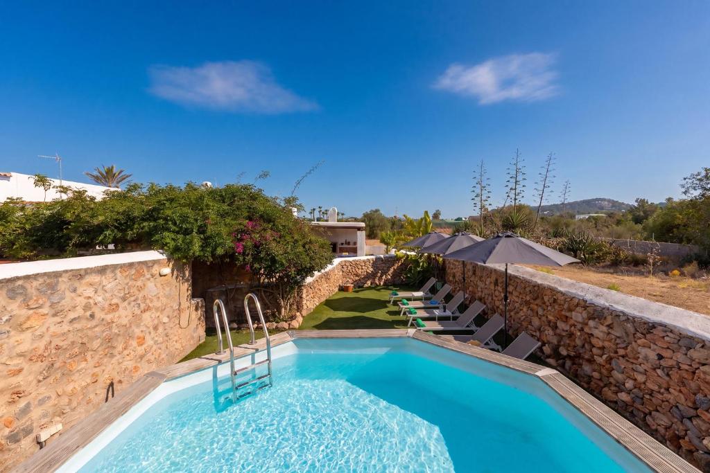 a pool with chairs and a stone wall at New! Villa Can Marsoch in Santa Eularia des Riu