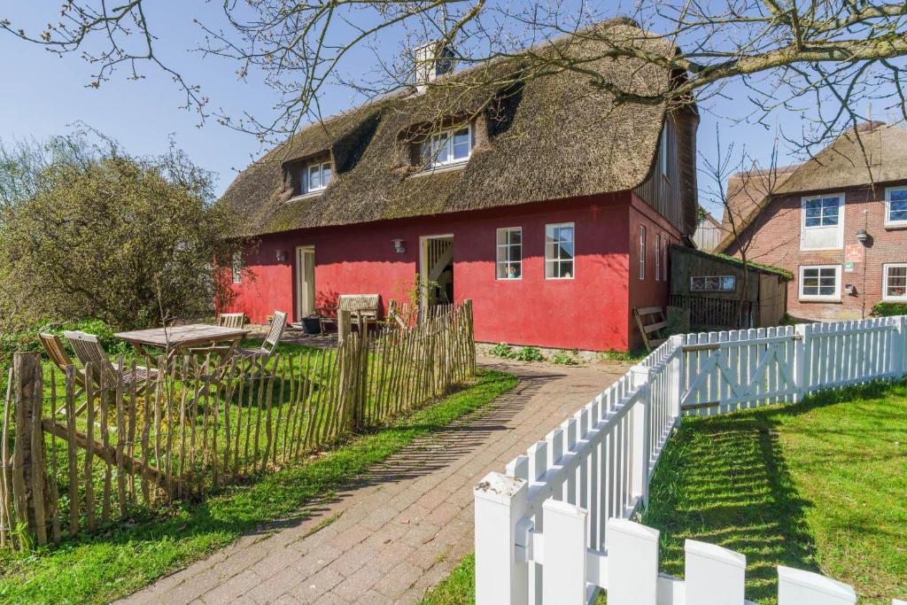 a red house with a thatched roof and a white fence at Haus Bei Der Kirche in Oland