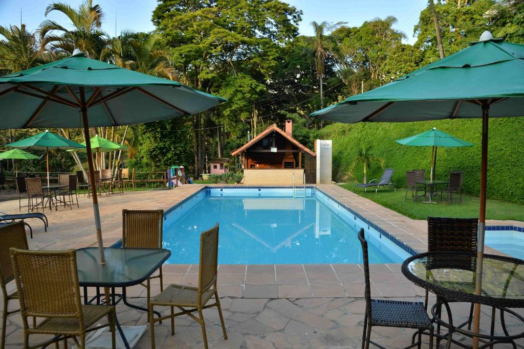 a swimming pool with tables and chairs and umbrellas at Hotel fazenda do Cedro in Areal