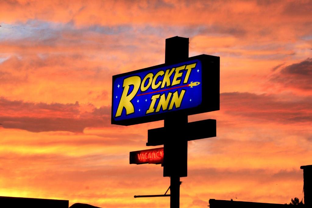 un panneau sur un poteau avec un coucher de soleil en arrière-plan dans l'établissement Rocket Inn, à Truth or Consequences