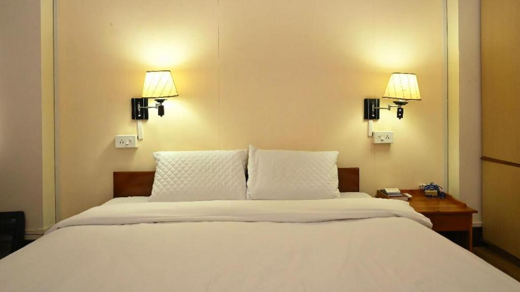 a bedroom with a white bed with two lights on the wall at Aijal Club in Āīzawl