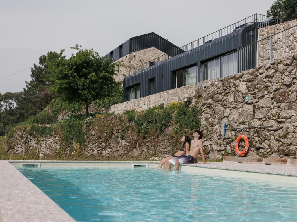 two women sitting on the side of a swimming pool at Quinta Cerca da Milhera in Ponte da Barca