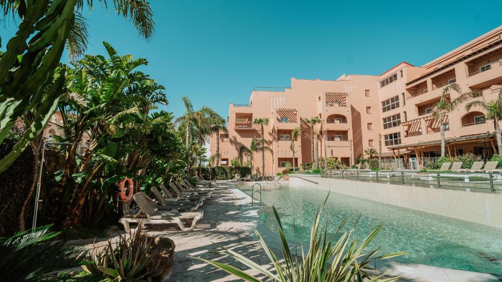 a swimming pool in a resort with palm trees and buildings at Hotel Tarifa Lances, a member of Radisson Individuals in Tarifa
