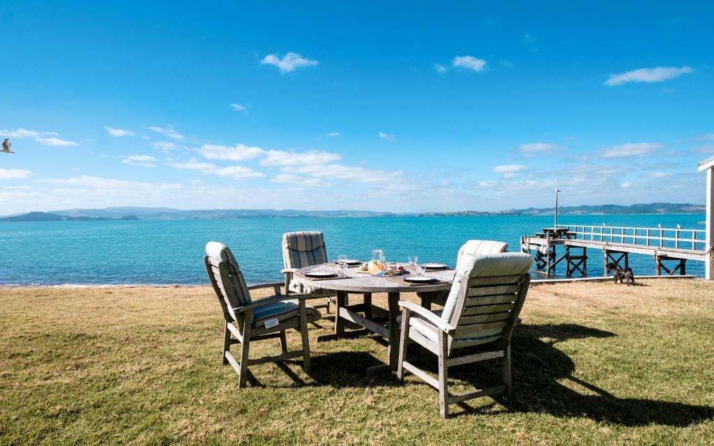 Waiheke Waters Edge في Omiha: طاولة وكراسي يجلسون على العشب بالقرب من الماء