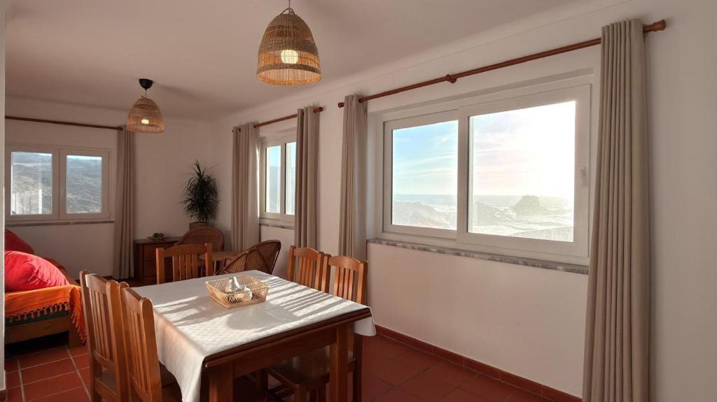 a dining room with a table and two windows at Apartamento sto estavão 2 in Zambujeira do Mar