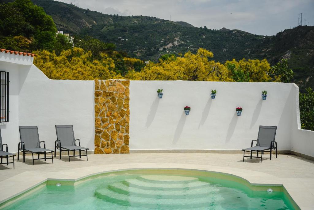 a swimming pool on a patio with chairs and a wall at Finca Tres Aguas, Casa Rural con Piscina Privada in Lanjarón