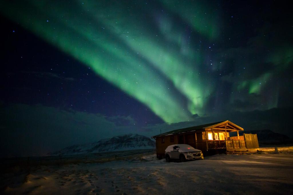 domek z samochodem zaparkowanym pod zorzą polarną w obiekcie Snorrastadir Farm Holidays w mieście Borgarnes