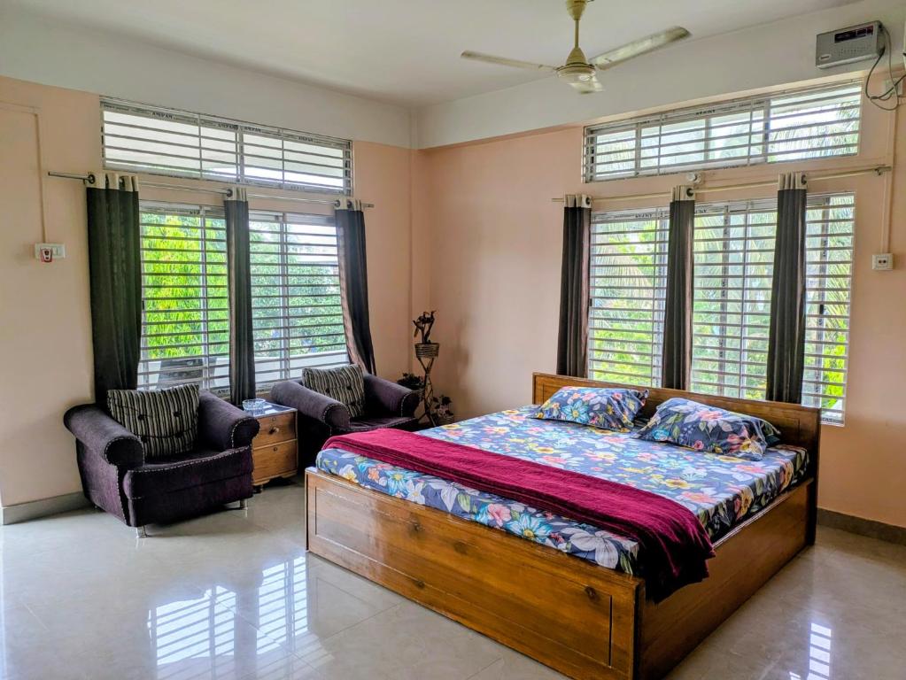a bedroom with a bed and two chairs and windows at Gogona Homestay in Guwahati