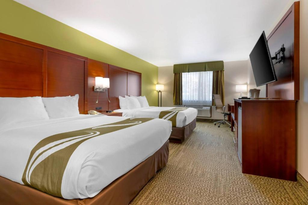 a hotel room with two beds and a flat screen tv at Quality Inn & Suites Stoughton - Madison South in Stoughton