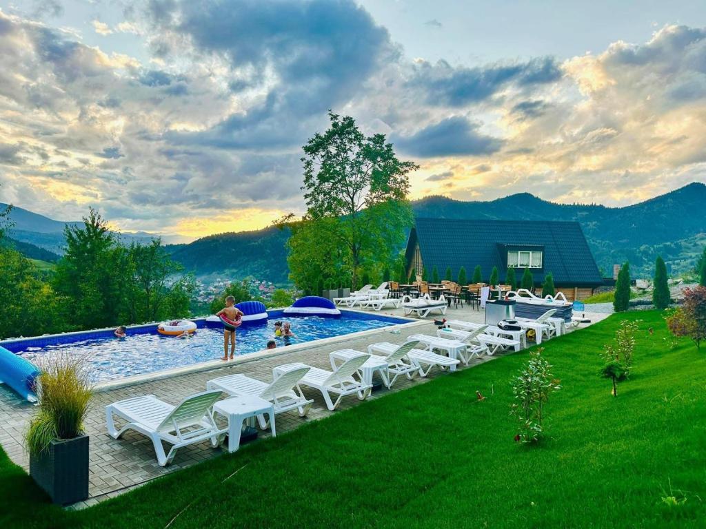 a pool with white lounge chairs next to a field at Doinita House in Borşa