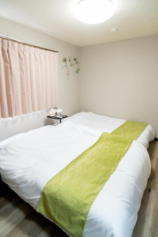 a bedroom with a white bed with a green blanket on it at Ijiri Relax stay in Fukuoka