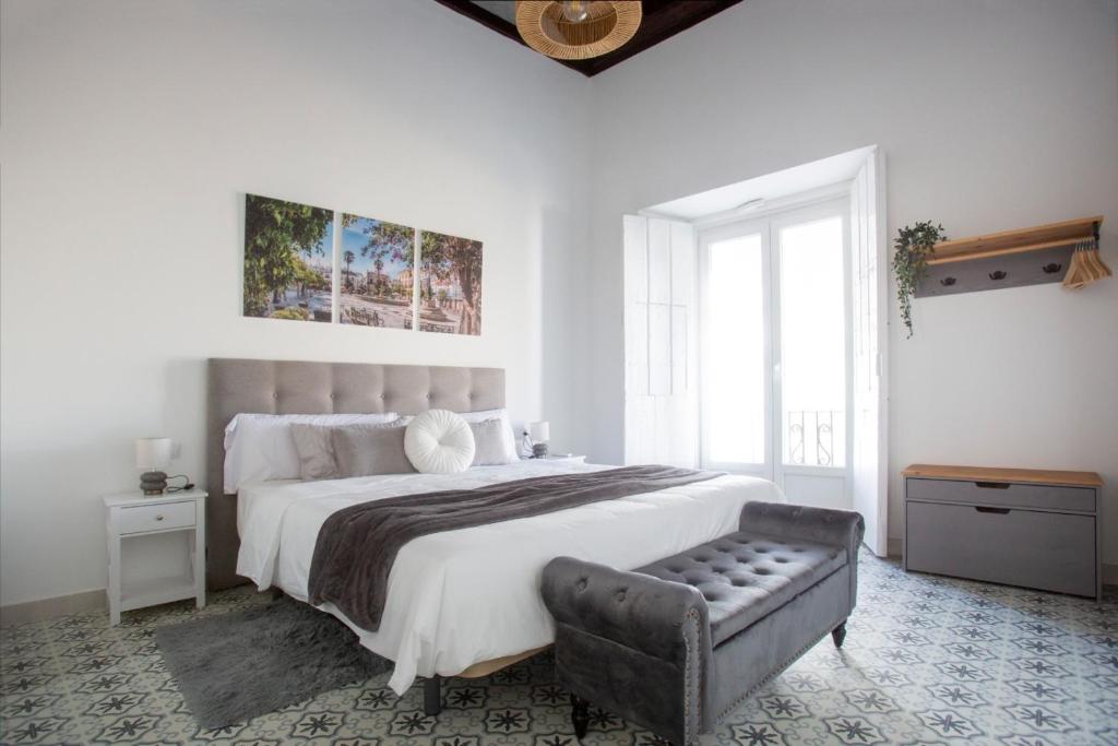 a white bedroom with a large bed and a chair at Hogar de la plata in Sanlúcar de Barrameda