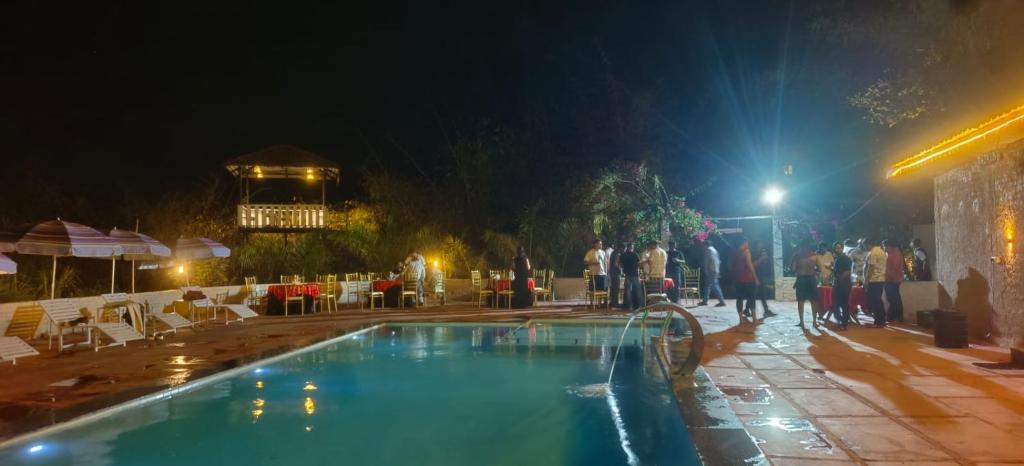 a group of people standing around a swimming pool at night at The Kiran's Resort Pench in Khawāsa