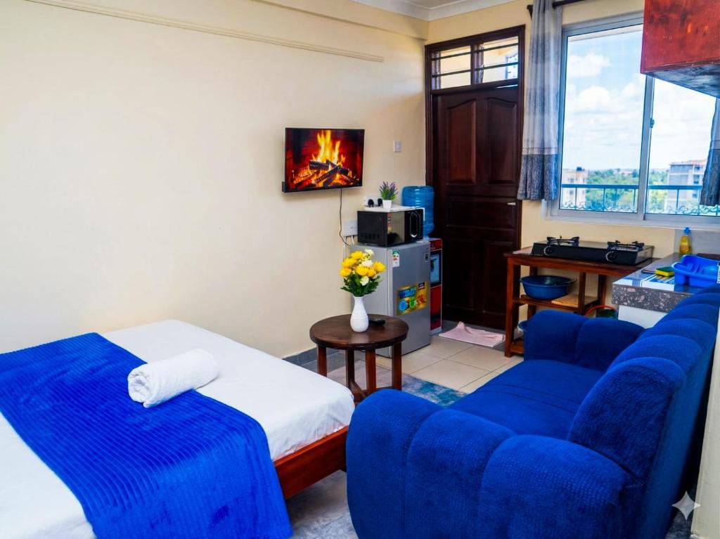 a living room with blue chairs and a bed and a tv at Dorado Homestay, Chaani in Mombasa