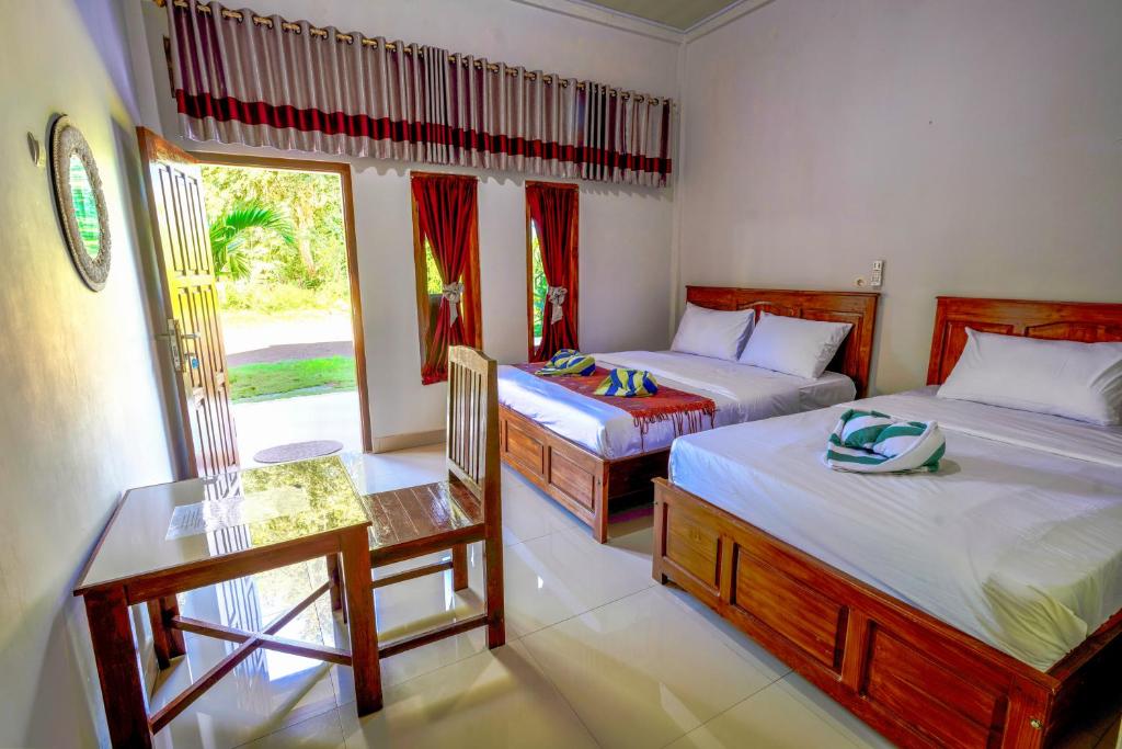 a bedroom with two beds and a table and a window at Golo Tango Homestay in Labuan Bajo