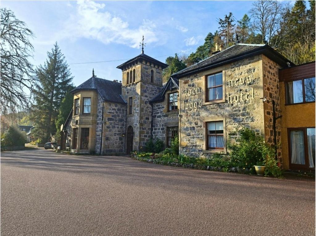 a large stone house with a tower on a street at Loch Ness Lodge Hotel in Drumnadrochit