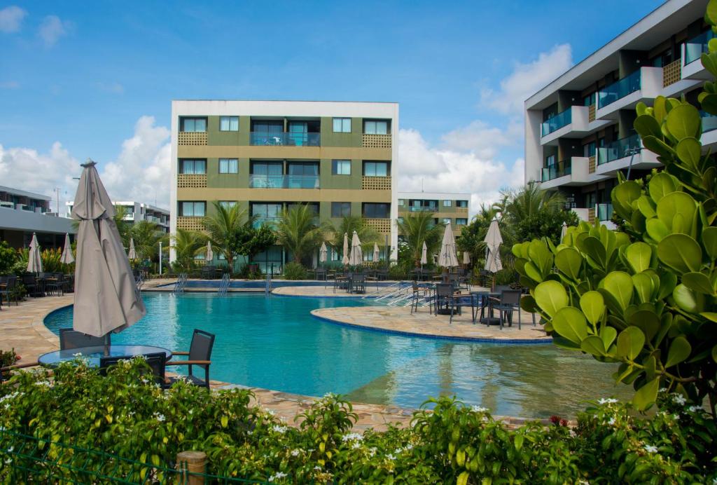 a swimming pool with tables and umbrellas in front of a building at Mana Beach Exclusive in Porto De Galinhas
