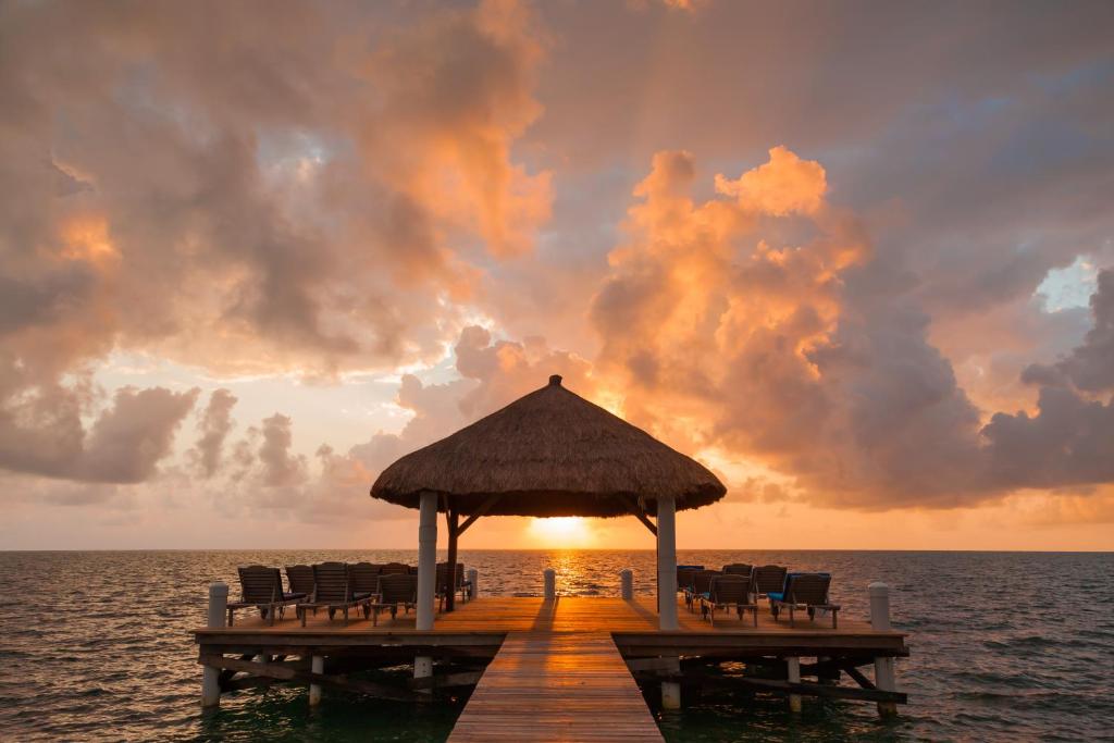 a pier in the ocean with chairs and a sunset at Weezie's Ocean Front Hotel and Garden Cottages in Caye Caulker