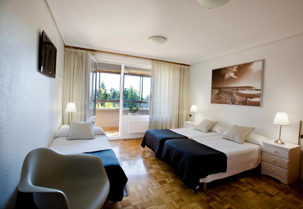 a bedroom with two beds and a chair and a window at Pensión Pasadena in Pamplona