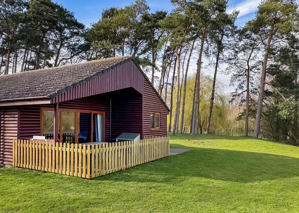 a small cabin with a fence in the grass at Woodland Waters in Ancaster