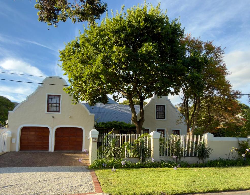 a white house with a white fence and a tree at Chinta Cottage Hermanus in Hermanus