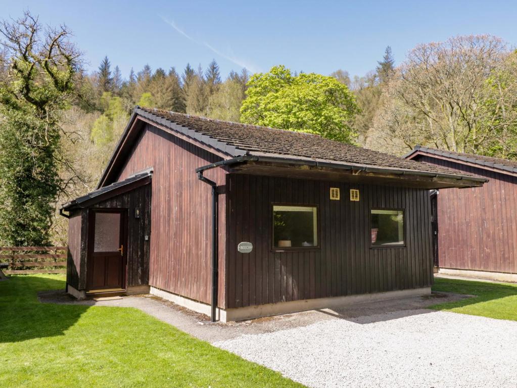 a brown barn with a door and a grass yard at Beech Timber Lodge in Keswick