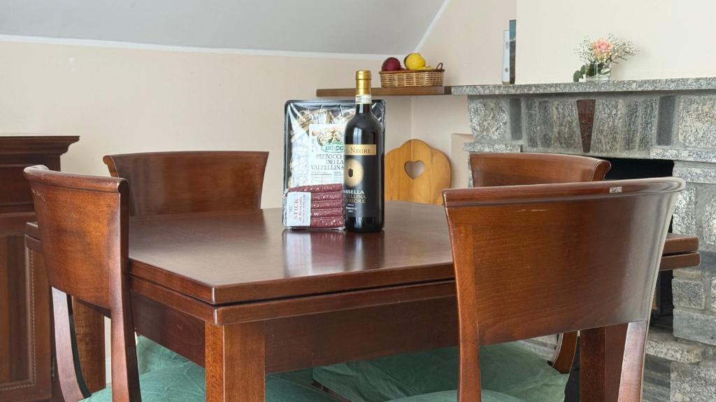 a bottle of wine on a wooden table with chairs at Appartamento Belvedere in Teglio