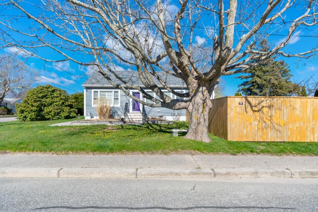 a house with a tree in front of a fence at Point Judith Coastal Retreat in Narragansett
