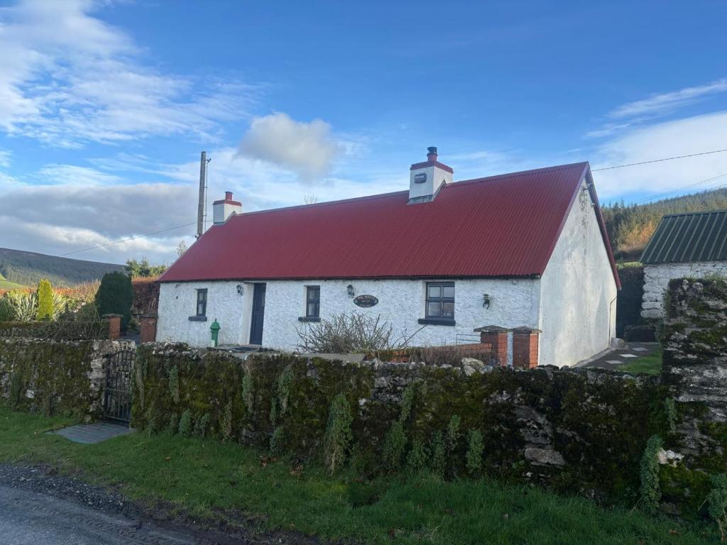 a white house with a red roof behind a stone fence at Mag Byrne's Cottage in Sandy Ford