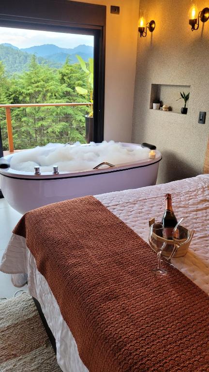 a bedroom with a large bed with a tub in a window at Casa Chalé dos Pinhas - Chalé Romântico e Aconchegante - Hidromassagem - Lareira - Vista da Montanha - Próximo a Campos do Jordão in Santo Antônio do Pinhal