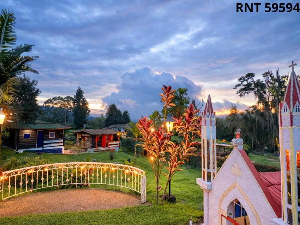 a home with a christmas light fence and a church at Cabañas rurales Aldea de Cabal - Naturaleza y Sabor cerca a Termales Reservamos tu entrada a termales Santa Rosa in Santa Rosa de Cabal