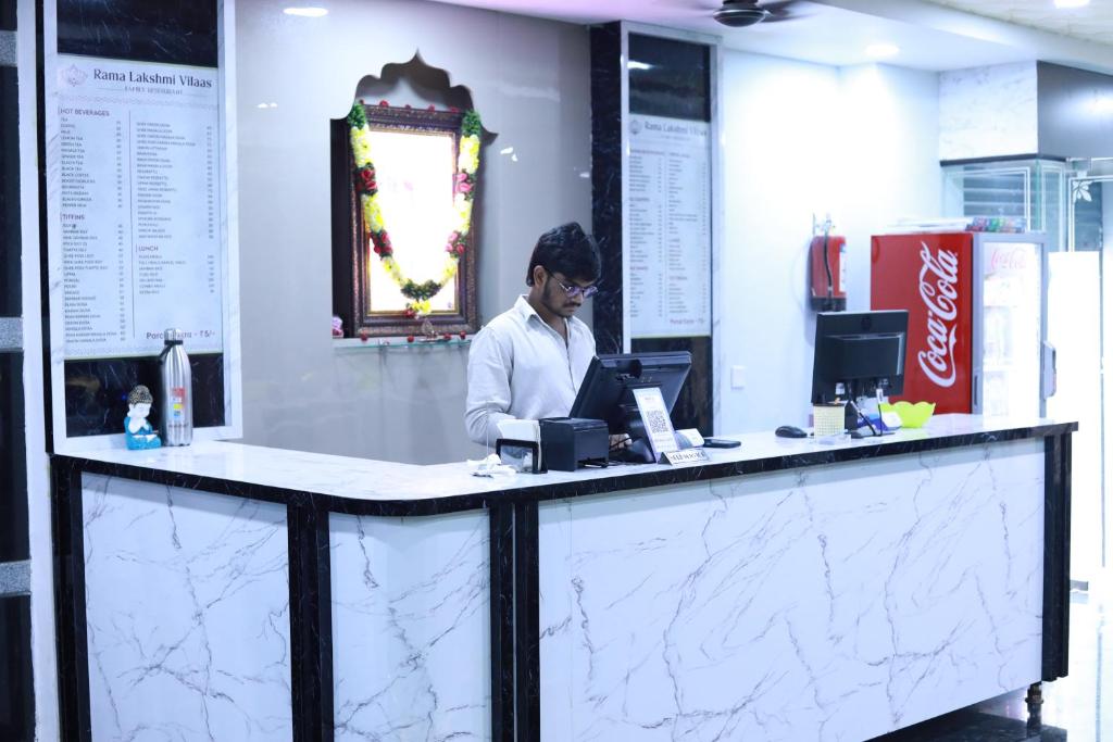 a person standing behind a counter with a computer at SRL Grand Residency in Tirupati