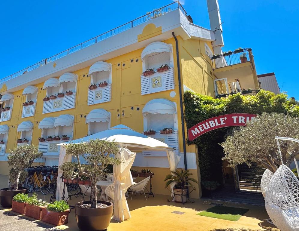 a yellow building with an umbrella and tables and trees at Meublè Tripoli in Grado