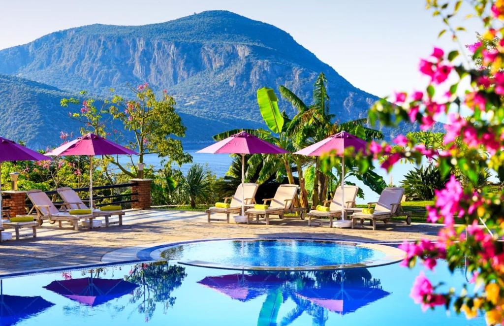 a pool with chairs and umbrellas and a mountain at Kalkan Regency in Kalkan