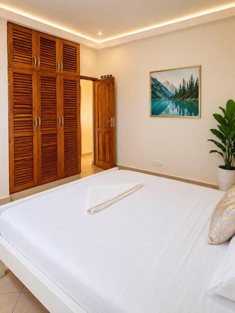 a large white bed in a bedroom with wooden cabinets at Evara Luxe stay in Mombasa