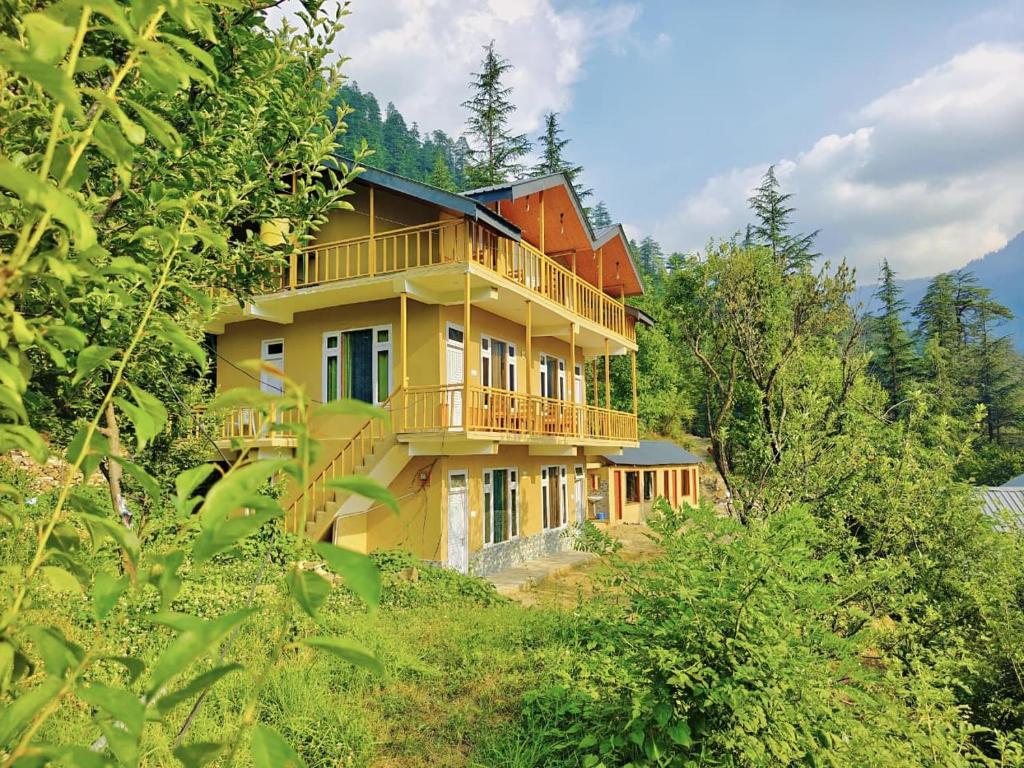 a large yellow house on a hill with trees at Sparrow Whisper in Jibhi