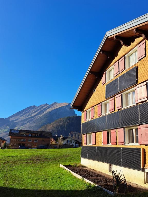 a building on a field with mountains in the background at Familienfreundliches Bregenzerwälderhaus in Au im Bregenzerwald