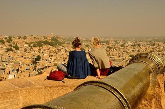 two people sitting on top of a cannon looking at a city at Golden Celestial haveli jaisalmer in Jaisalmer