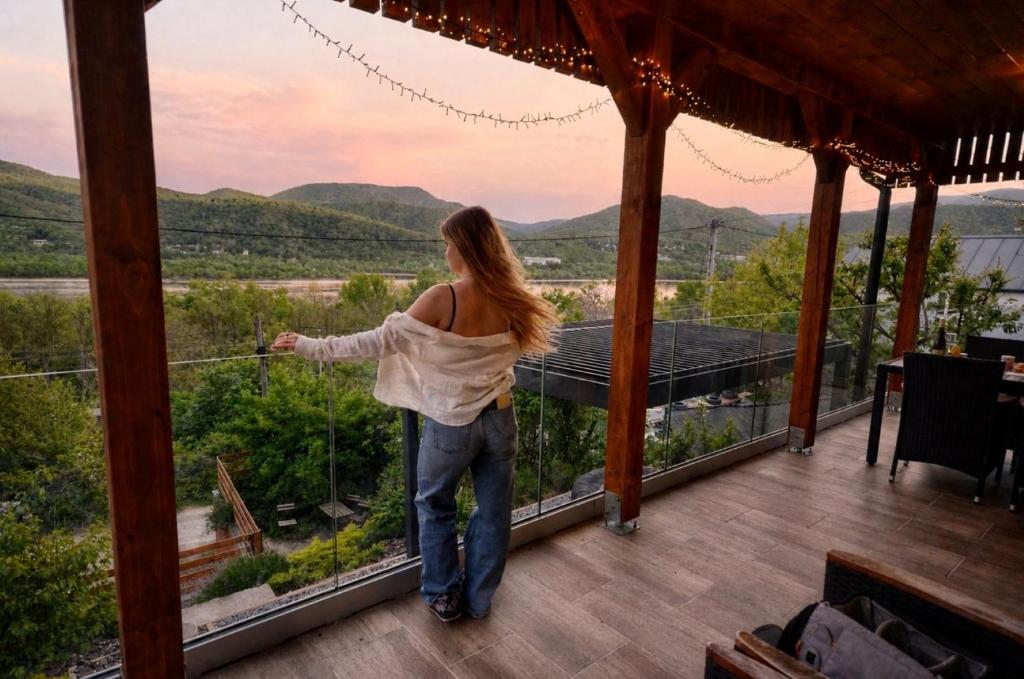 a woman standing on a porch looking out at the mountains at Aranyos Házikó in Nagymaros