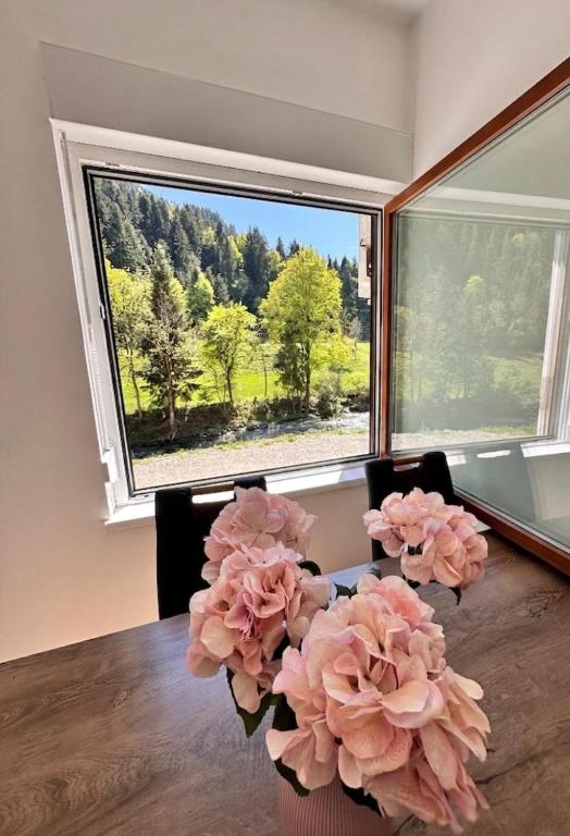 a room with a table with pink flowers in front of a window at Rina Apartments, Cozy Riverside Stay in Luče, near Logar Valley in Luče