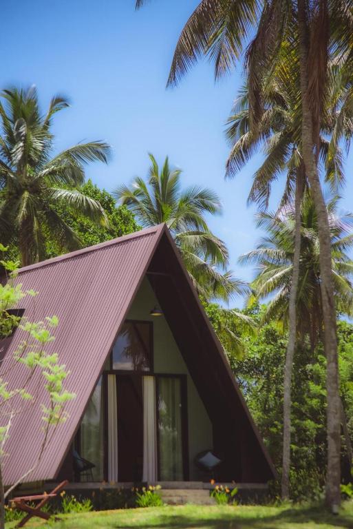 a small house with a pitched roof and palm trees at Hideout Boomeru in Matale
