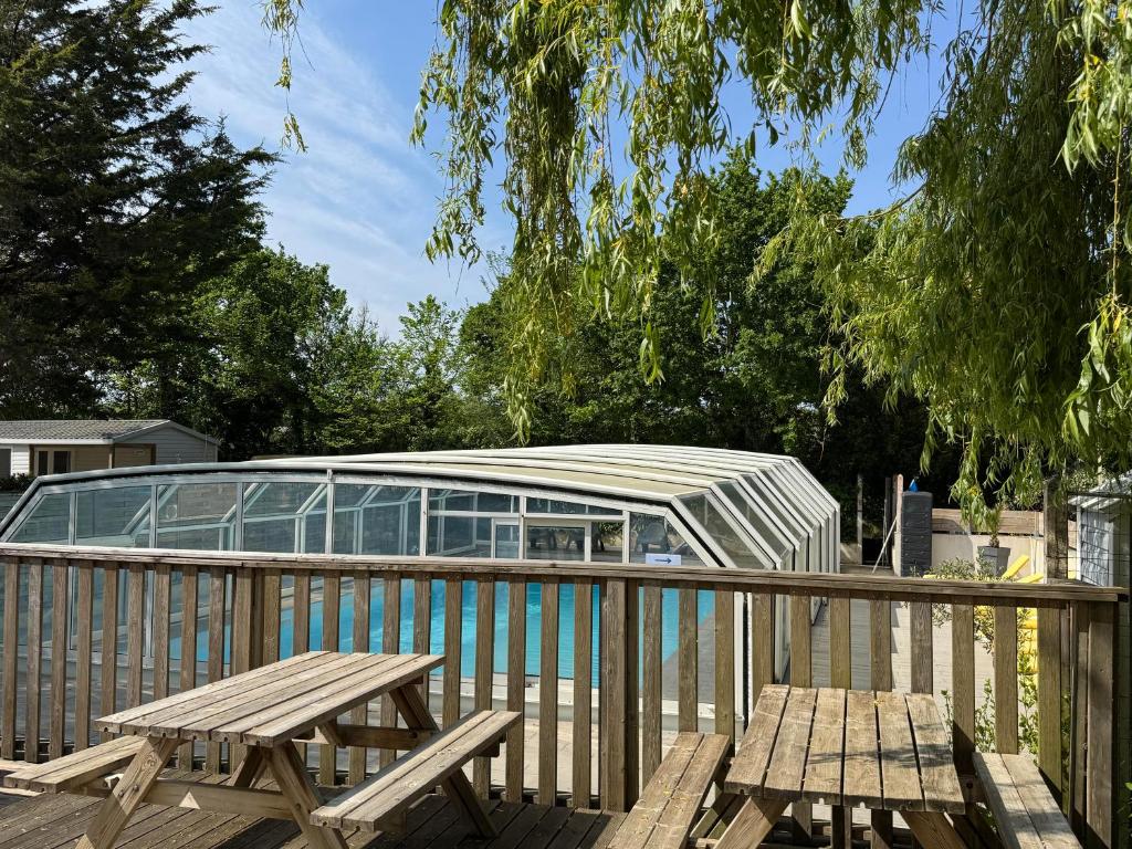 a deck with two picnic tables and a glass building at Camping Le Neptune in Lanloup